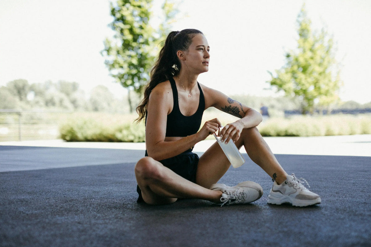 Femme en tenue de sport assise au sol, une gourde à la main