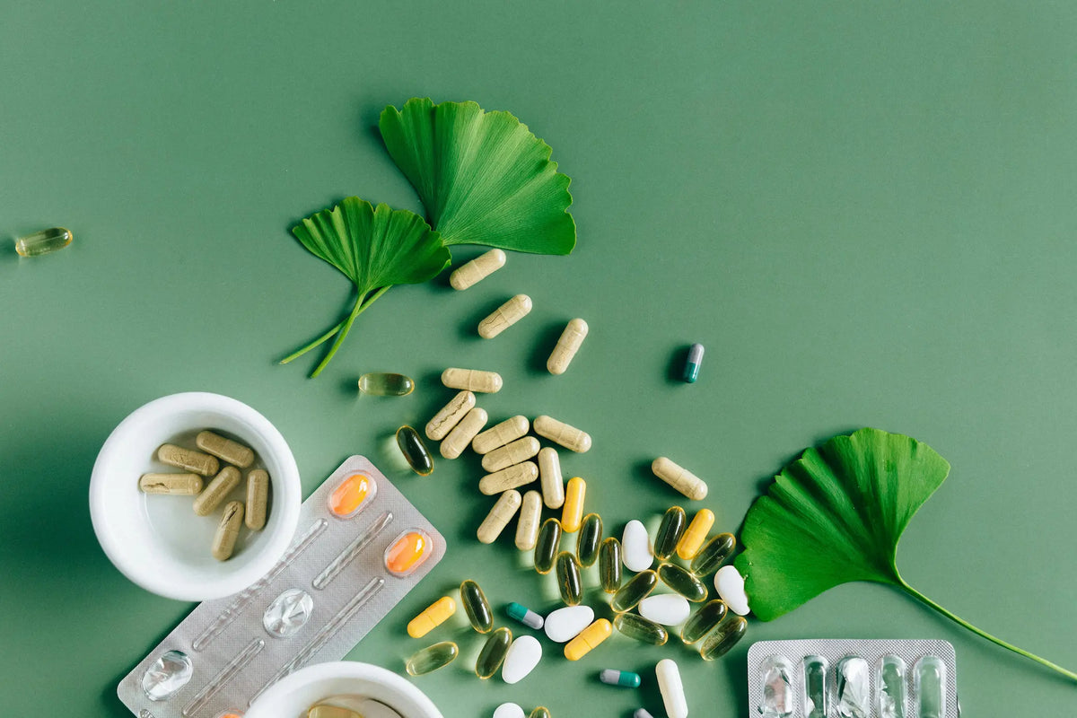Gélules, capsules et comprimés de compléments alimentaires sur fond vert, avec des feuilles de ginkgo