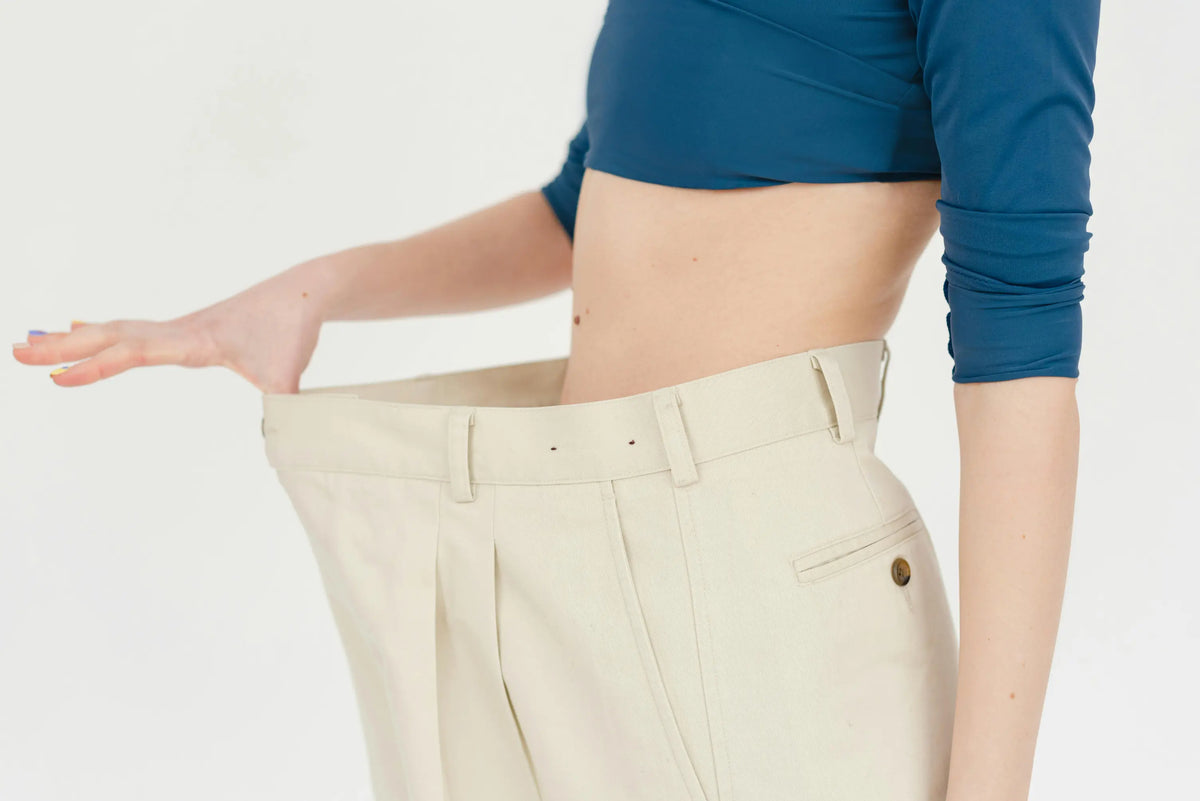 Femme qui écarte la ceinture d'un pantalon beige trop large