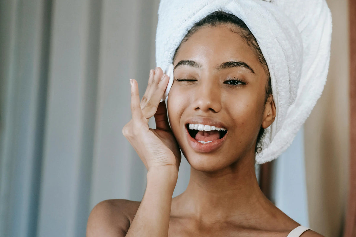 Femme souriante avec une serviette sur la tête, la main posée près de l'œil